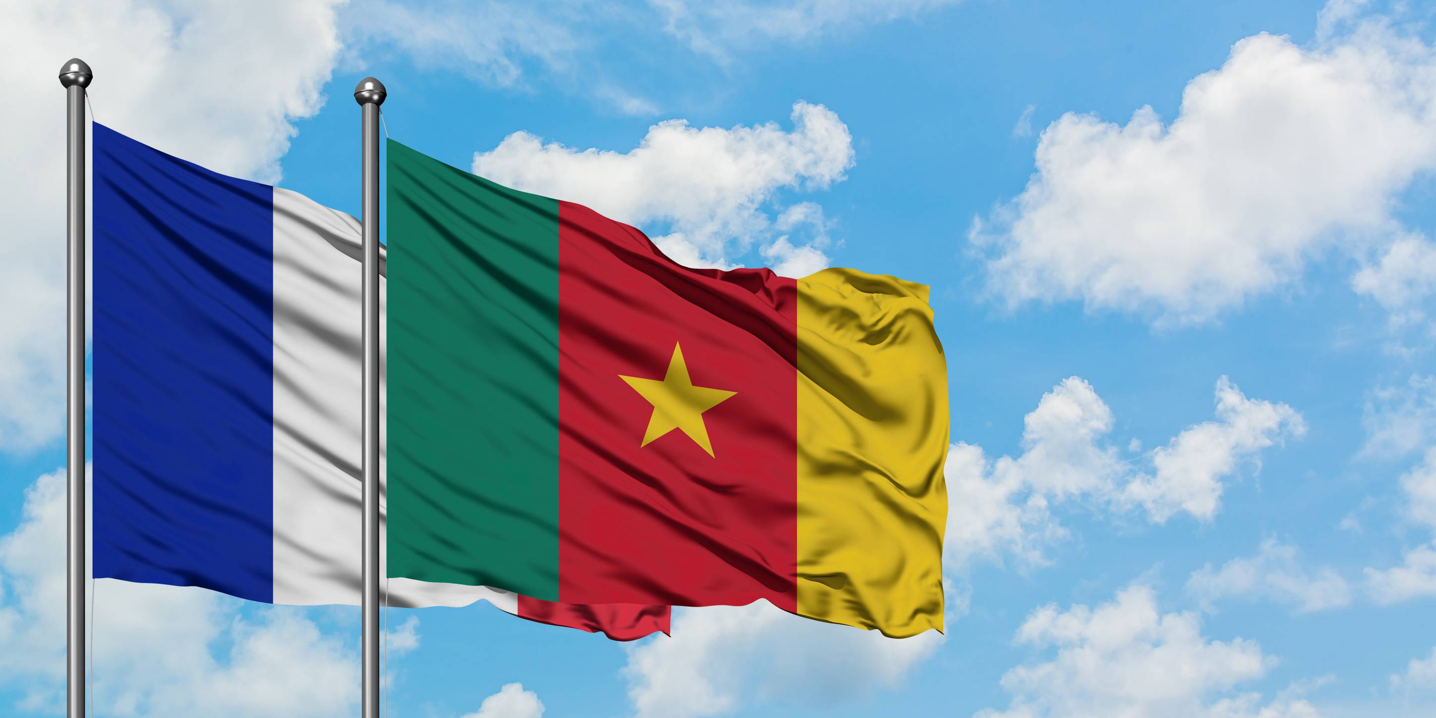 France And Cameroon Flag Waving In The Wind Against White Cloudy Blue Sky Together
